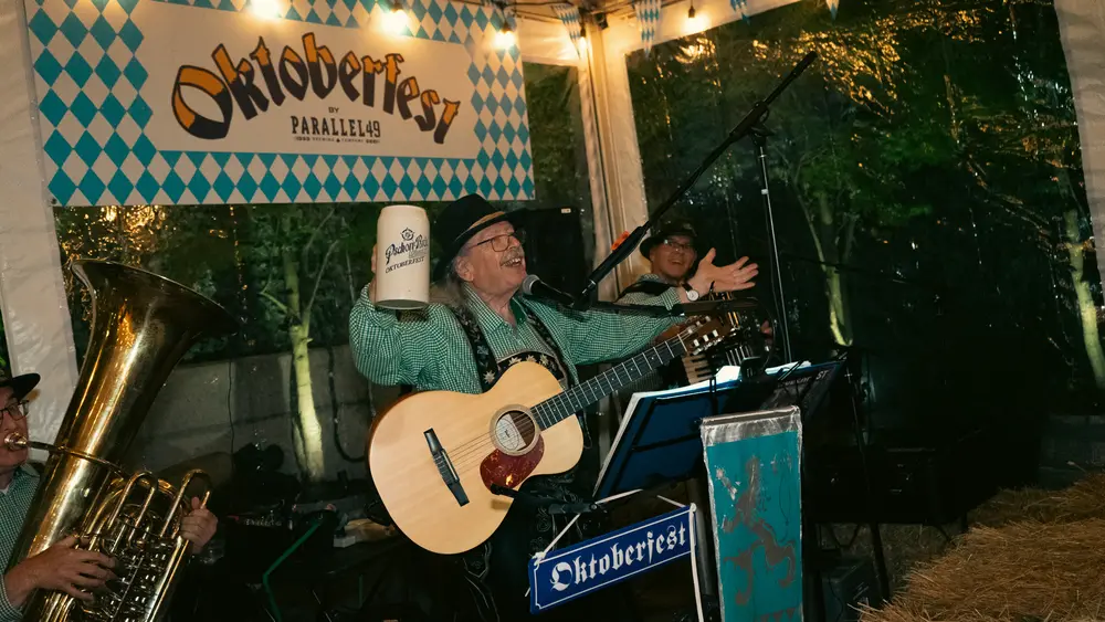 The Oktoberfest band playing guitar and tuba under an Oktoberfest banner