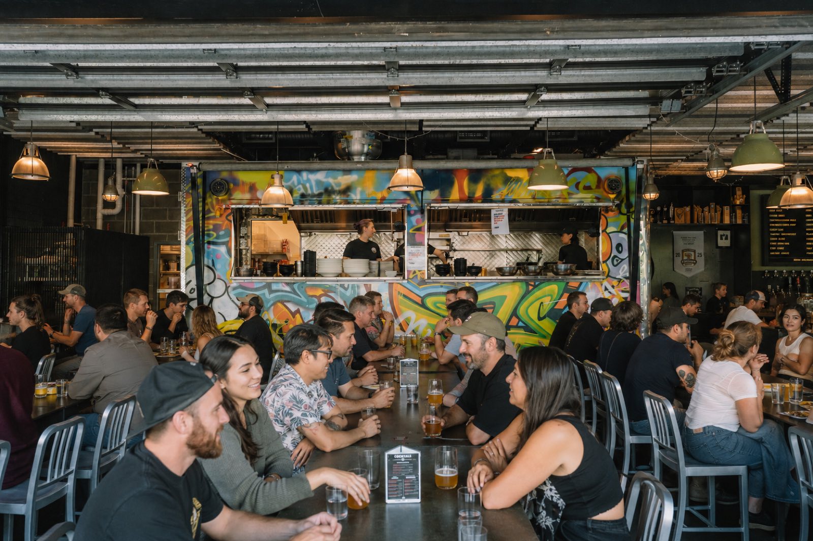 A busy Parallel 49 Street Kitchen — communal tables full of guests in front of the graffiti-covered indoor food truck